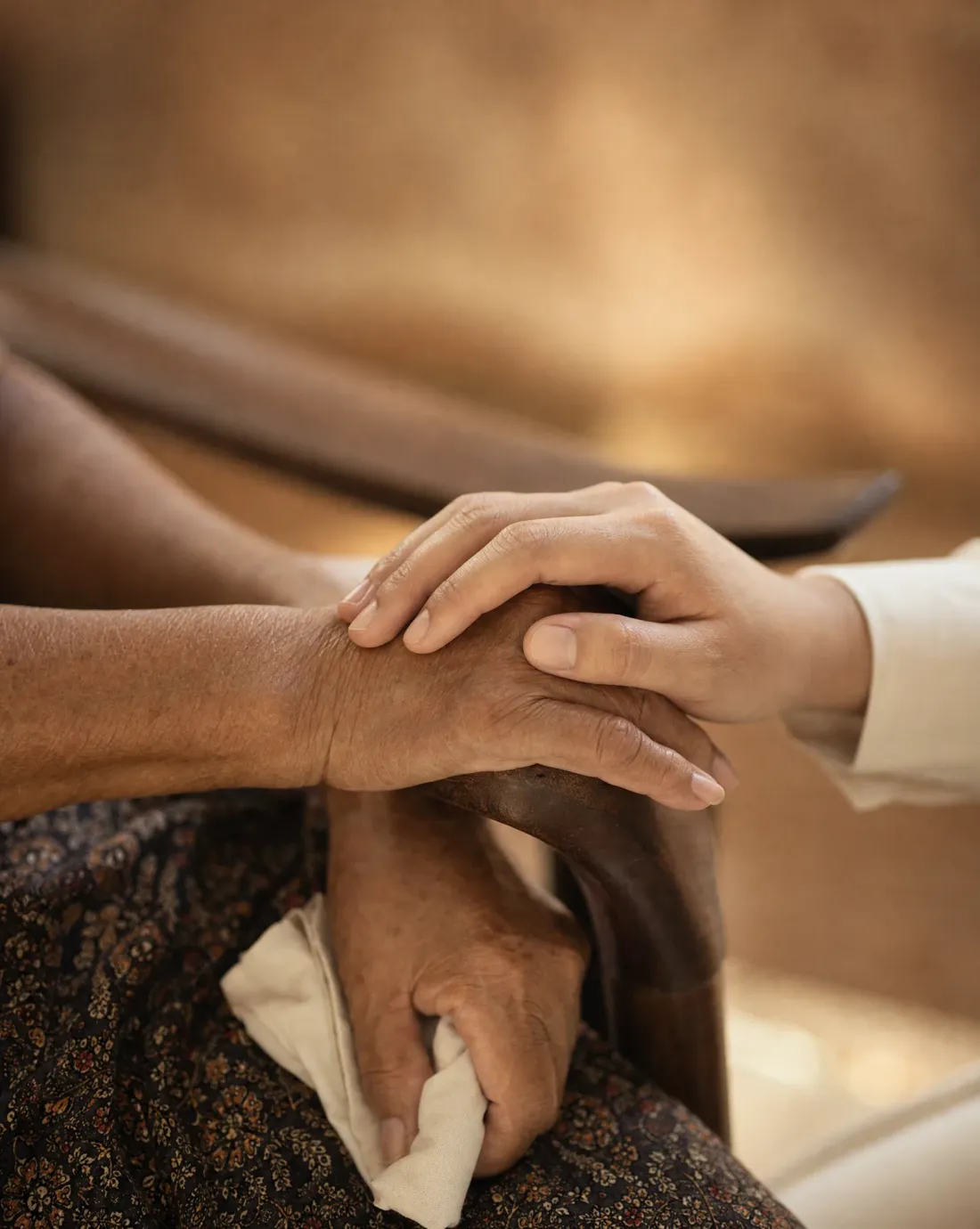 A younger hand resting gently on the hand of a community elder, a moment of care